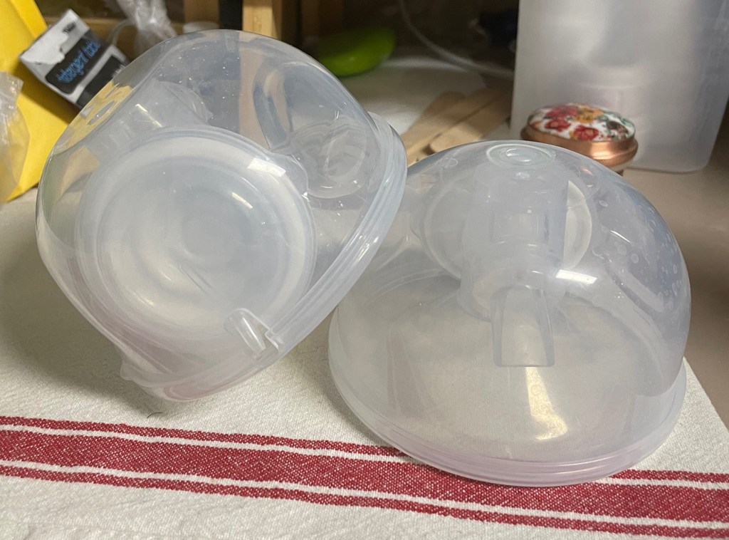The third image displays clear plastic breast pump shields laid out on a striped towel. These are typically components of a breast pump, used to assist with milk extraction during breastfeeding. The background contains kitchen storage items, suggesting the setting is within a home environment.